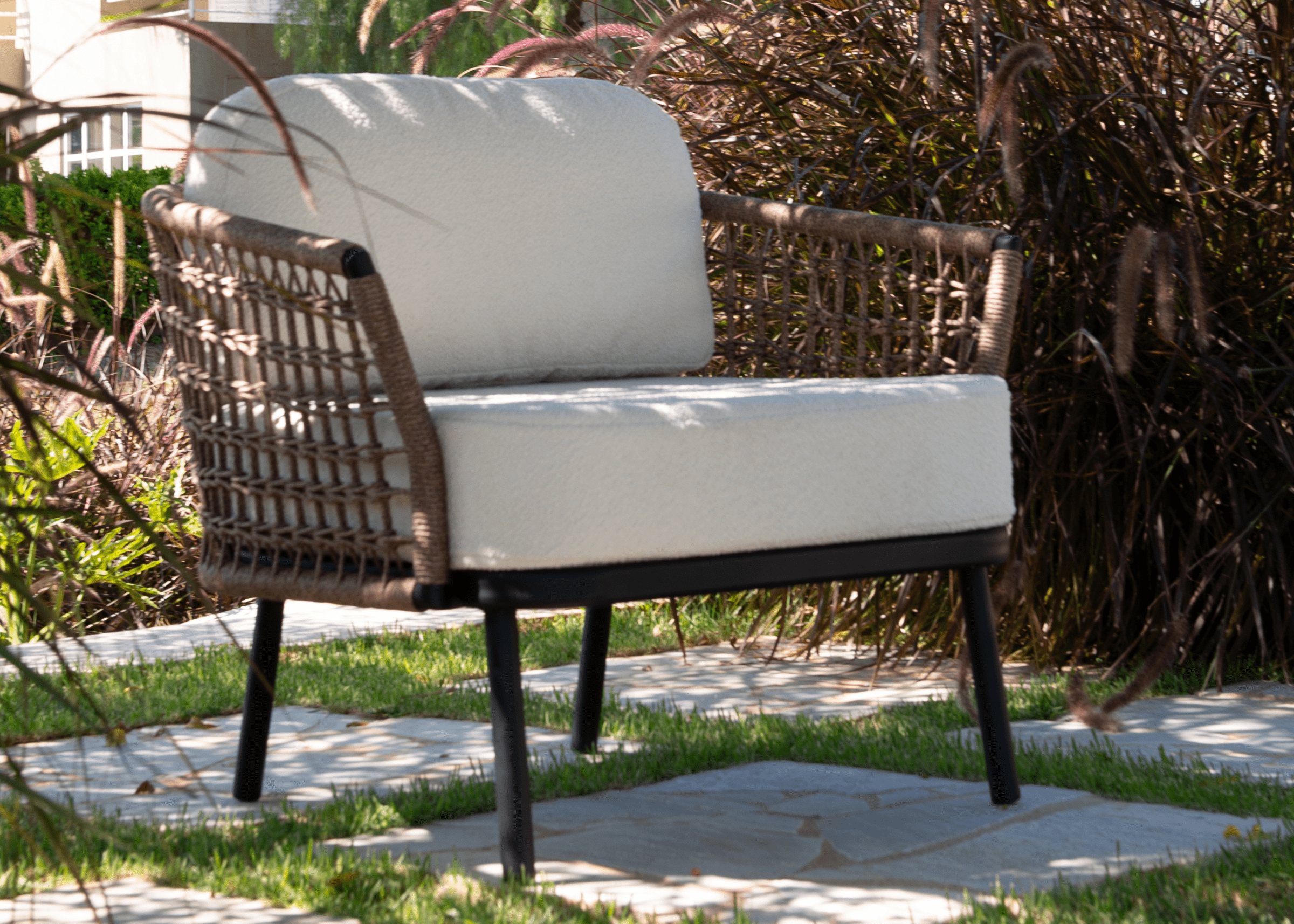 Poltrona Essence posicionada em jardim com iluminação natural e vegetação ao fundo.
