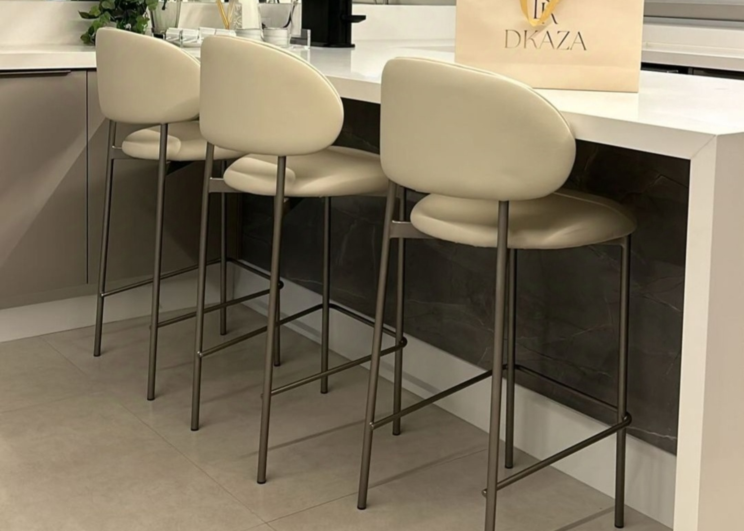 Banqueta Doralt com base em aço carbono e estofado em tecido off white, ambientada em cenário moderno. Móvel sofisticado e confortável para bancadas e áreas gourmet elegantes.