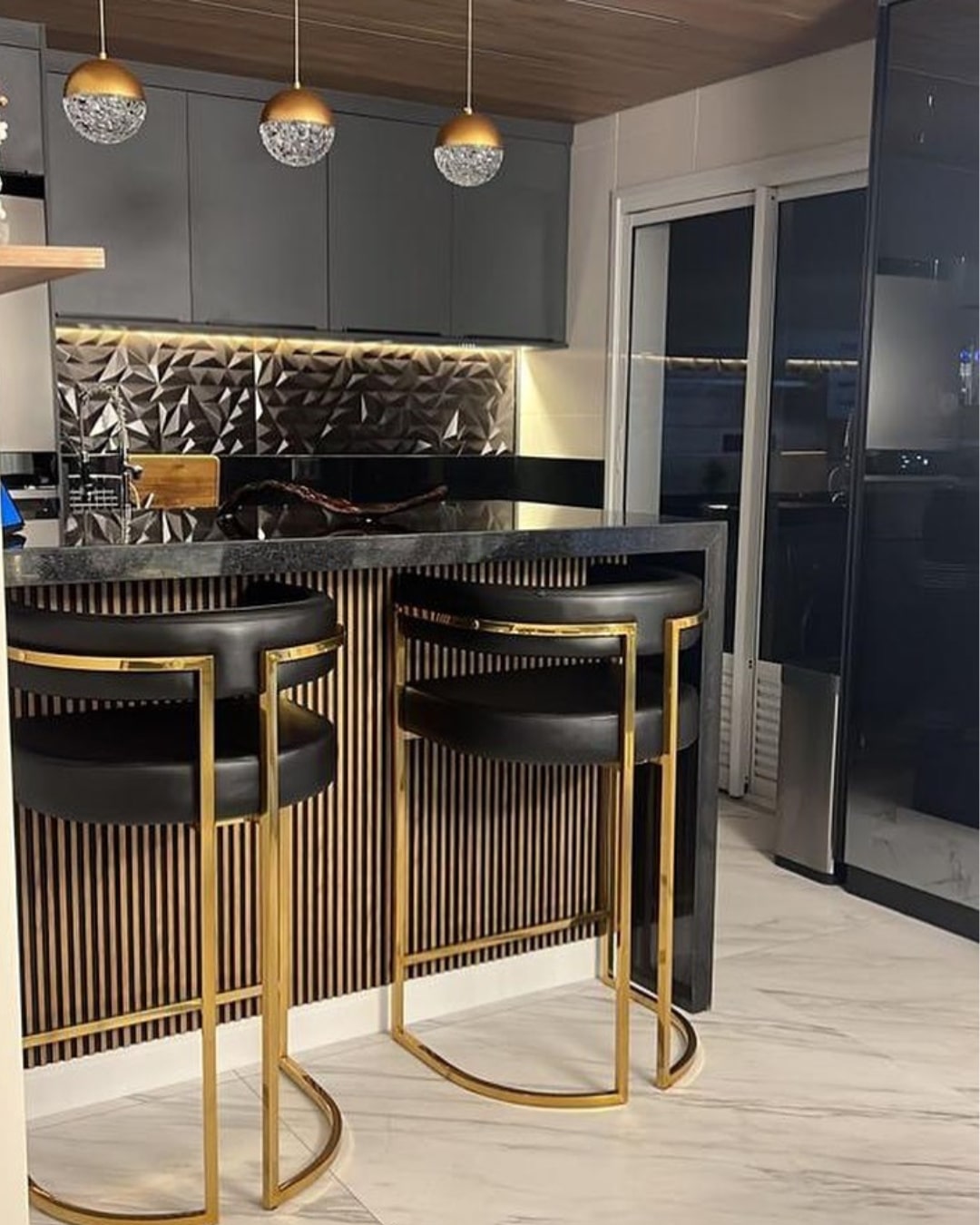 Banquetas Eldorado com estofado comuníssimo preto e base dourada em cozinha integrada de luxo.