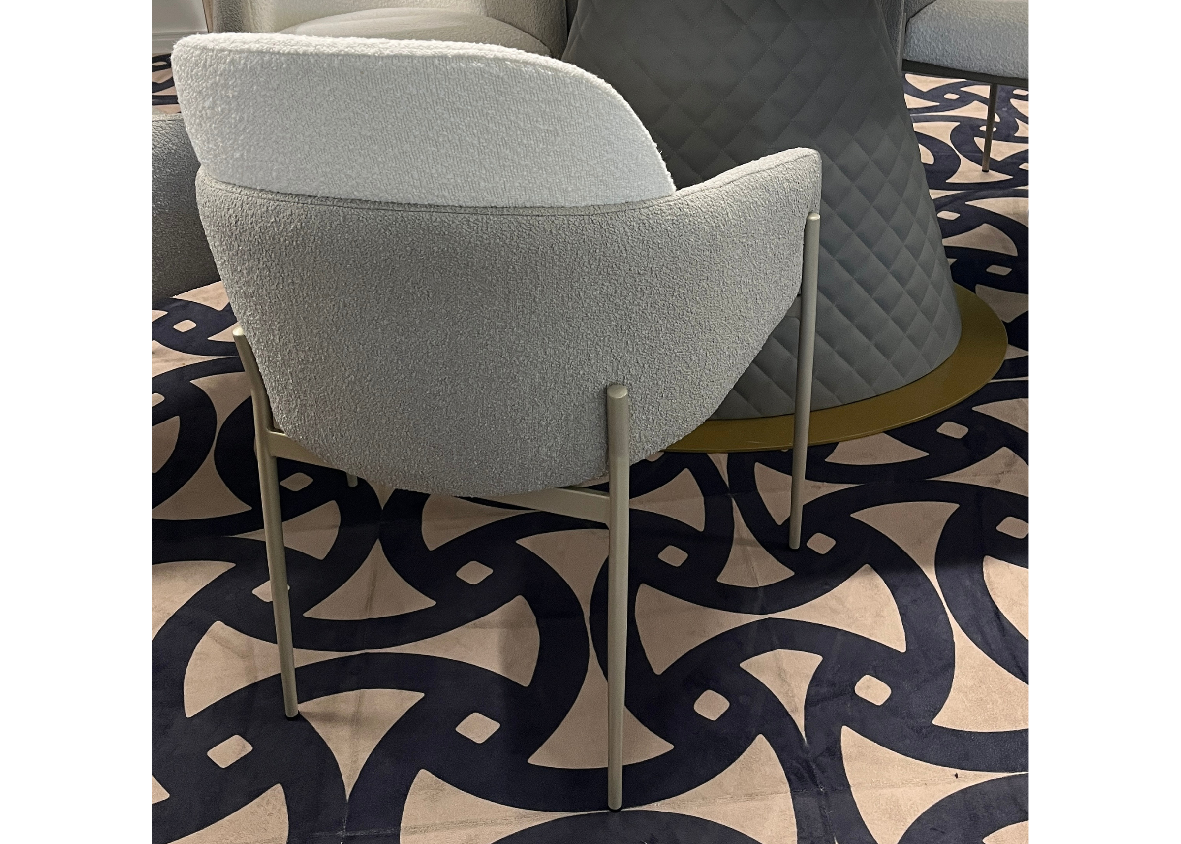 Cadeira Camelia em tecido bouclê off-white com detalhes em cinza, ambientada em cenário sofisticado. Móvel elegante e confortável para salas de jantar refinadas.