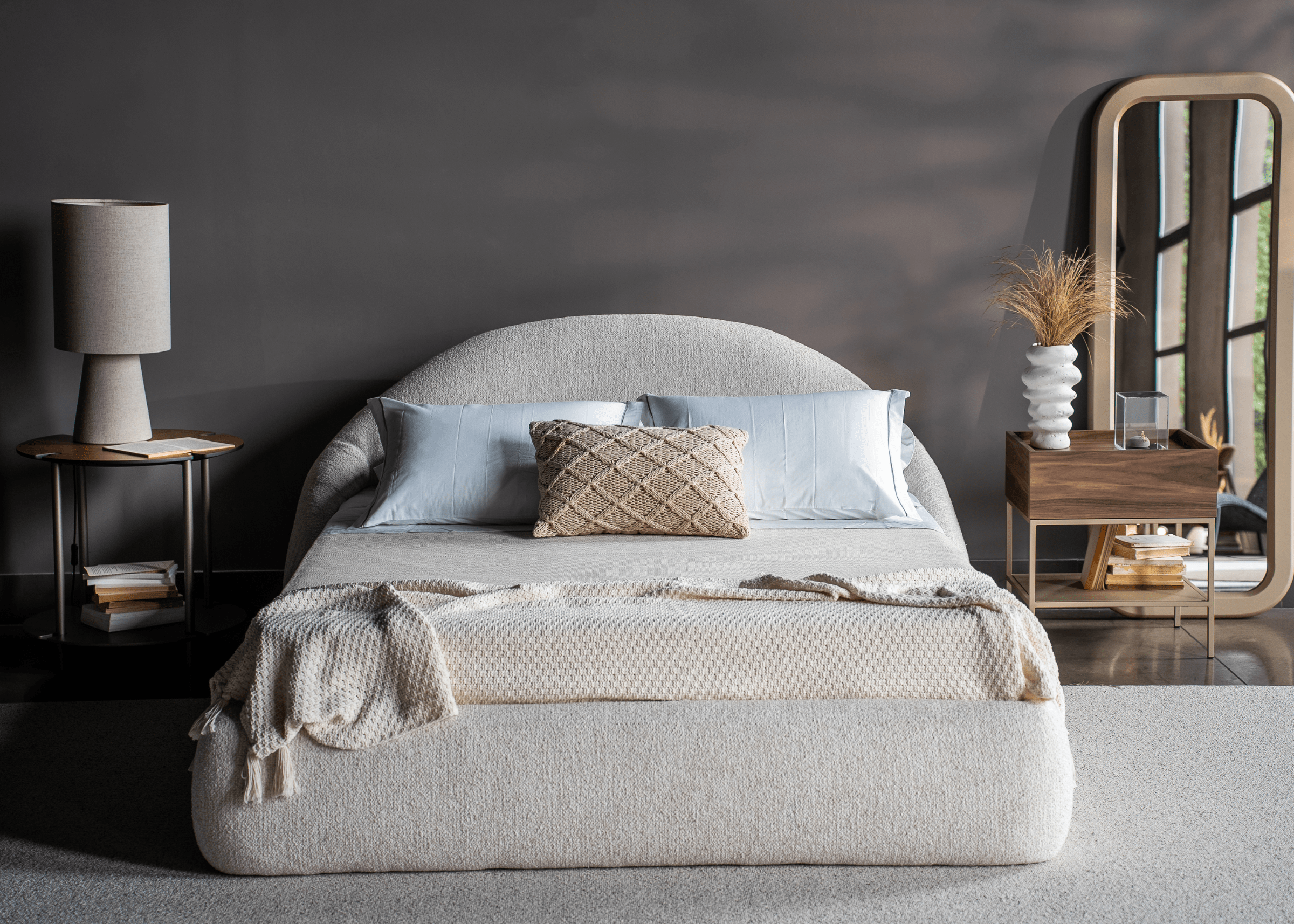 Cama Amira com estrutura estofada em tecido claro com cabeceira curva e design orgânico e acabamento suave, destacando conforto e volumetria.