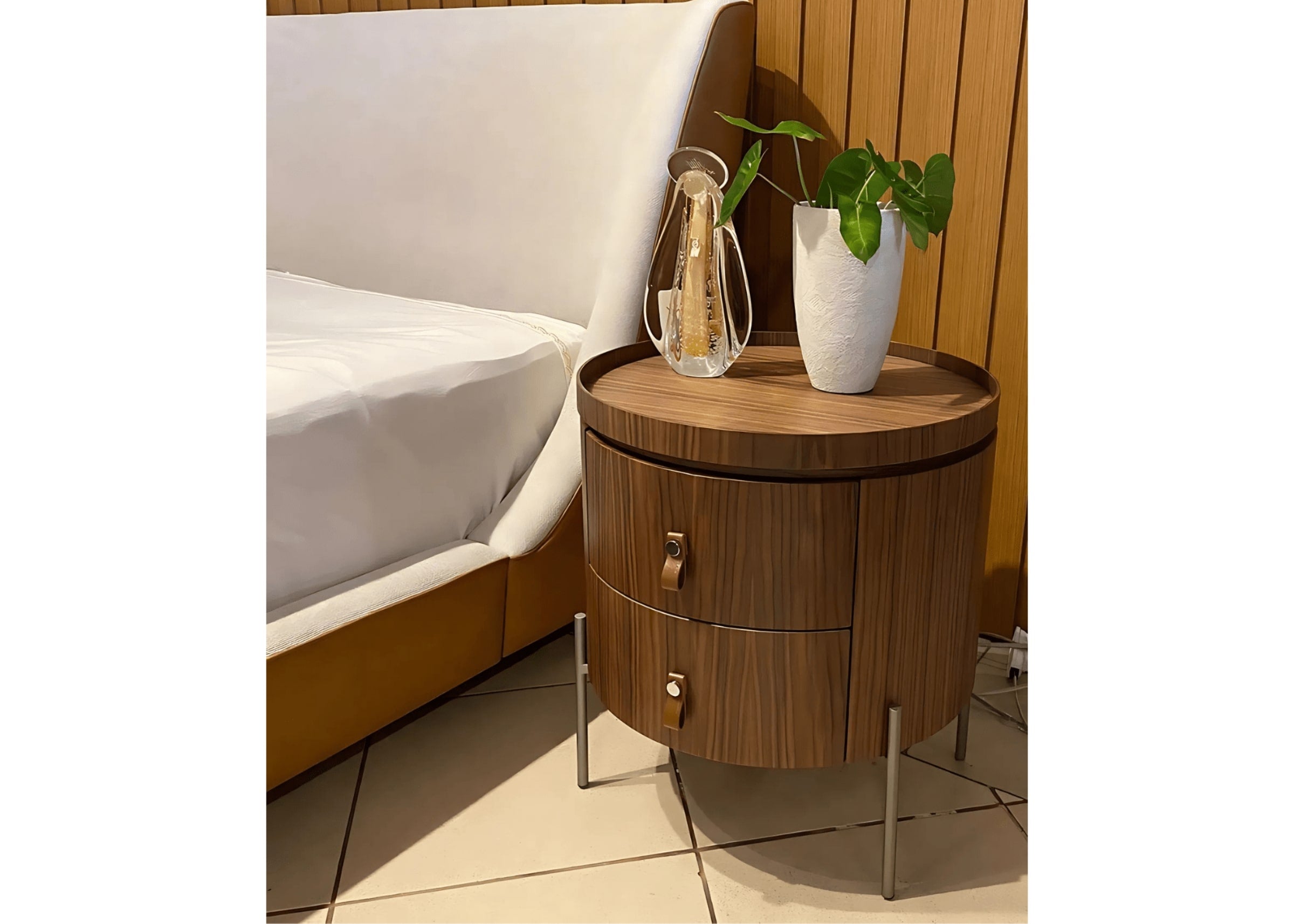 Criado-mudo redondo em madeira cinamomo com dois gavetões e puxadores em couro, em quarto sofisticado.