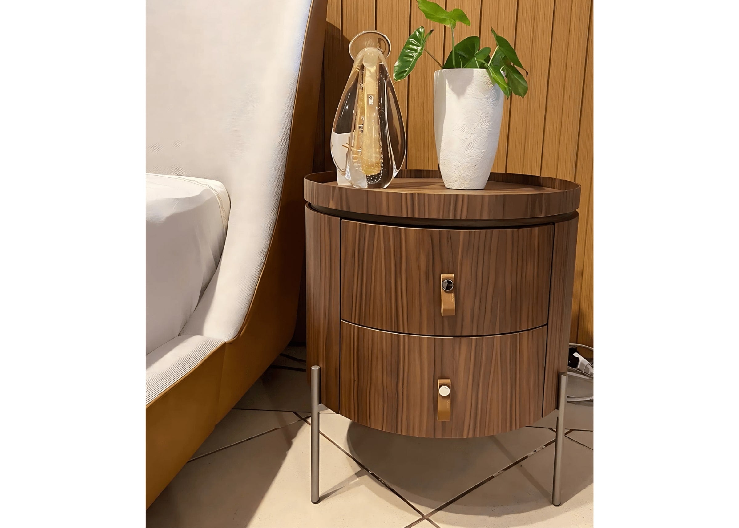 Mesa de cabeceira redonda em madeira cinamomo com gavetas e puxadores em couro, ao lado da cama.