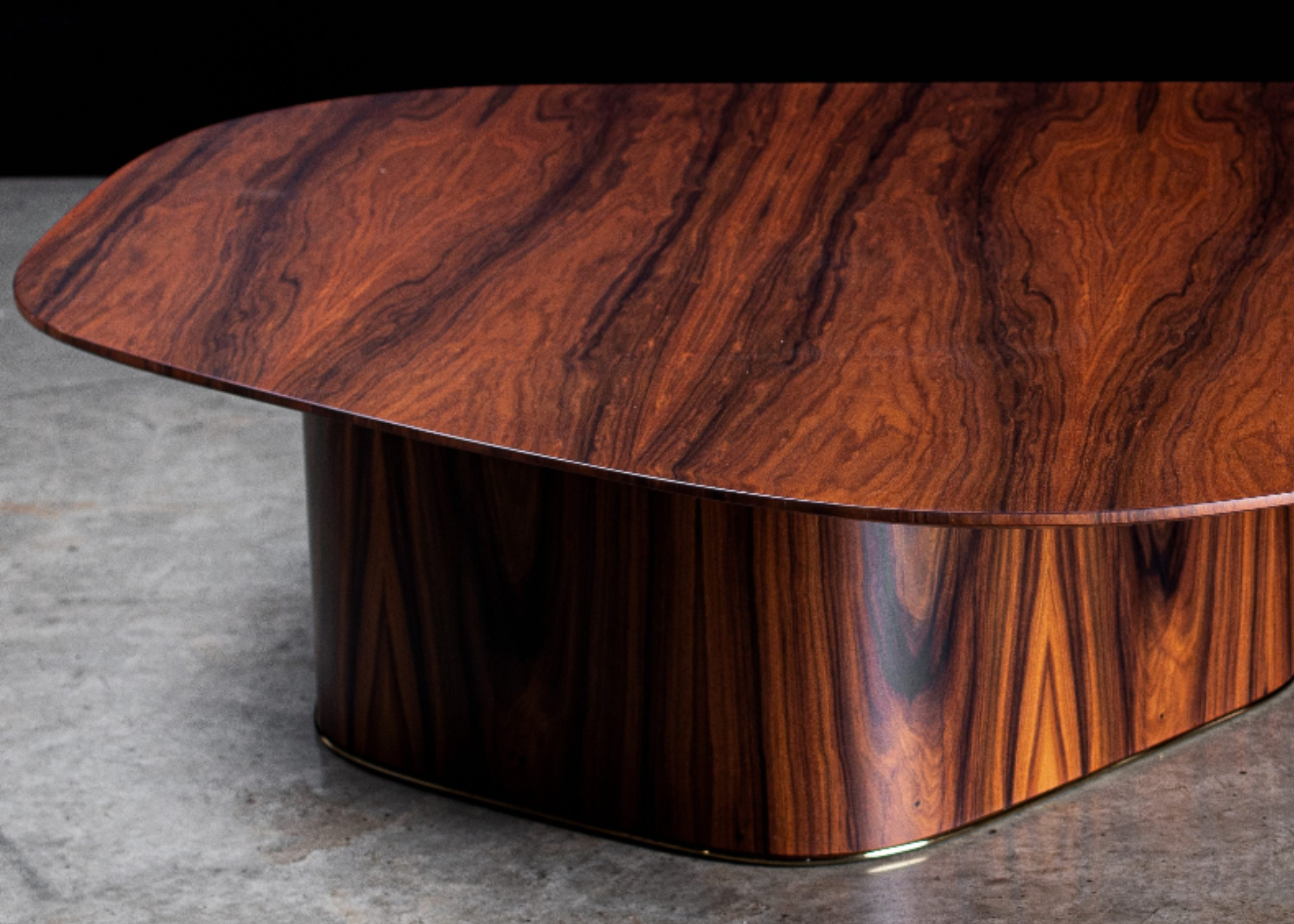 Mesa de centro modelo Delta com tampo orgânico em madeira Pau-Ferro e detalhe decorativo. Design elegante e contemporâneo, apresentada sobre fundo preto.