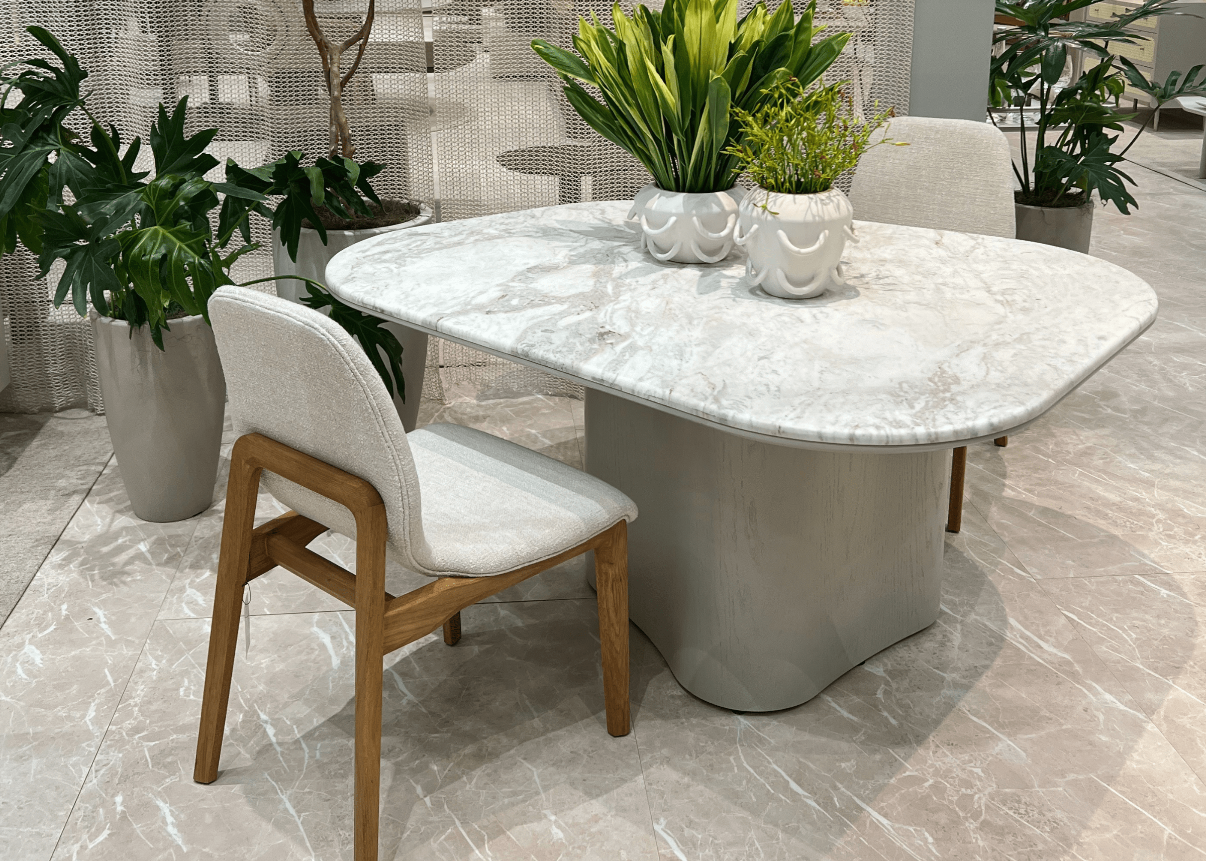 Mesa de Jantar Glen com tampo em mármore branco e borda off white, ambientada com cadeiras estofadas em tecido claro.
