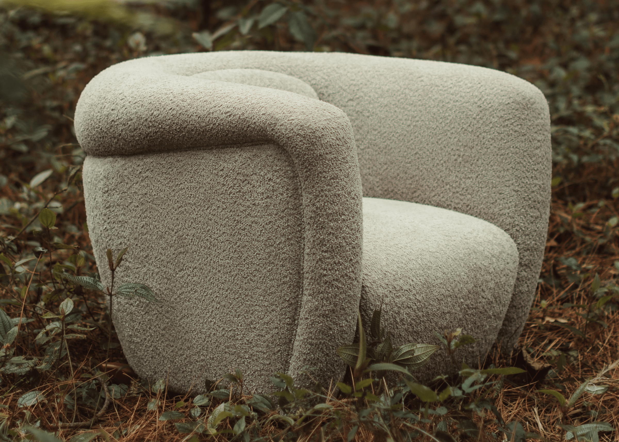 Poltrona Argos revestida em bouclé de tom neutro com base em madeira, destacada em ambiente corporativo elegante.