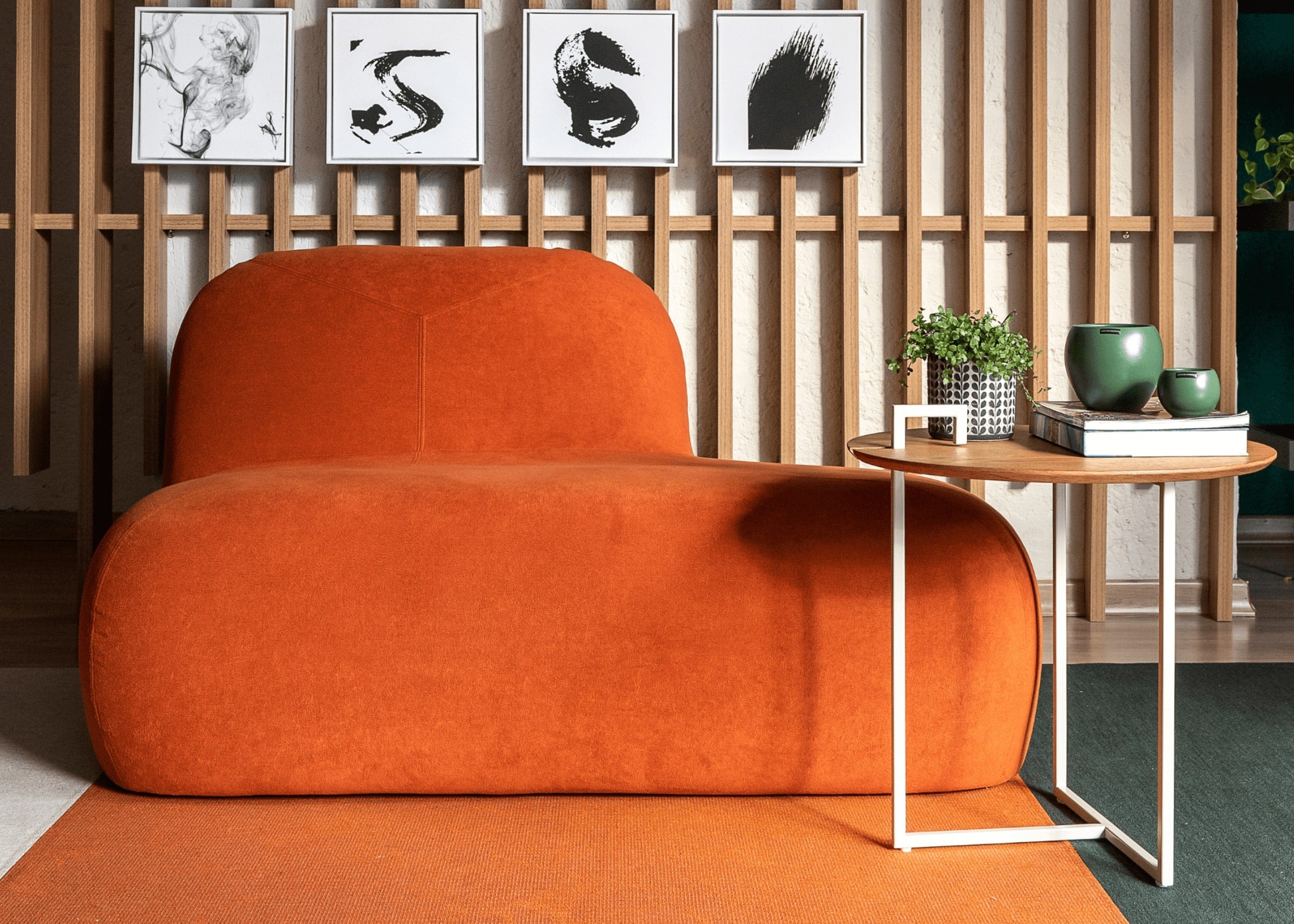 Poltrona Kumura com Avanço em tecido laranja, ambientada em sala moderna. Design arredondado e assento estendido com visual escultural para uma decoração elegante.