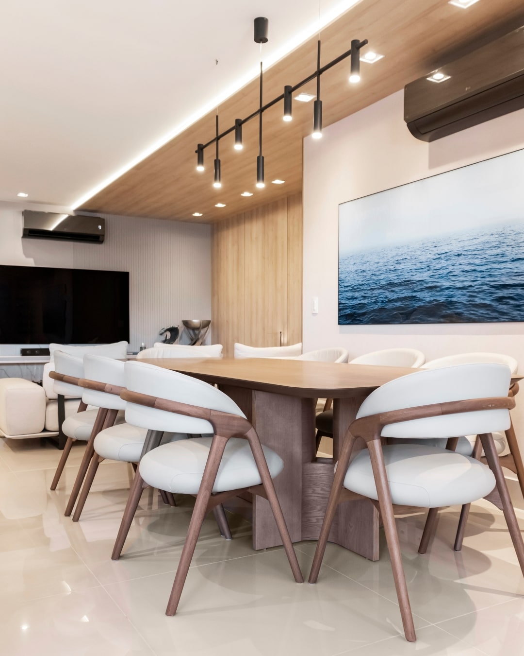 Sala de jantar moderna com mesa orgânica, cadeiras Eros estofadas em madeira e iluminação linear – ambiente sofisticado criado por Natalia Bialecki com móveis da Moveca Decor.