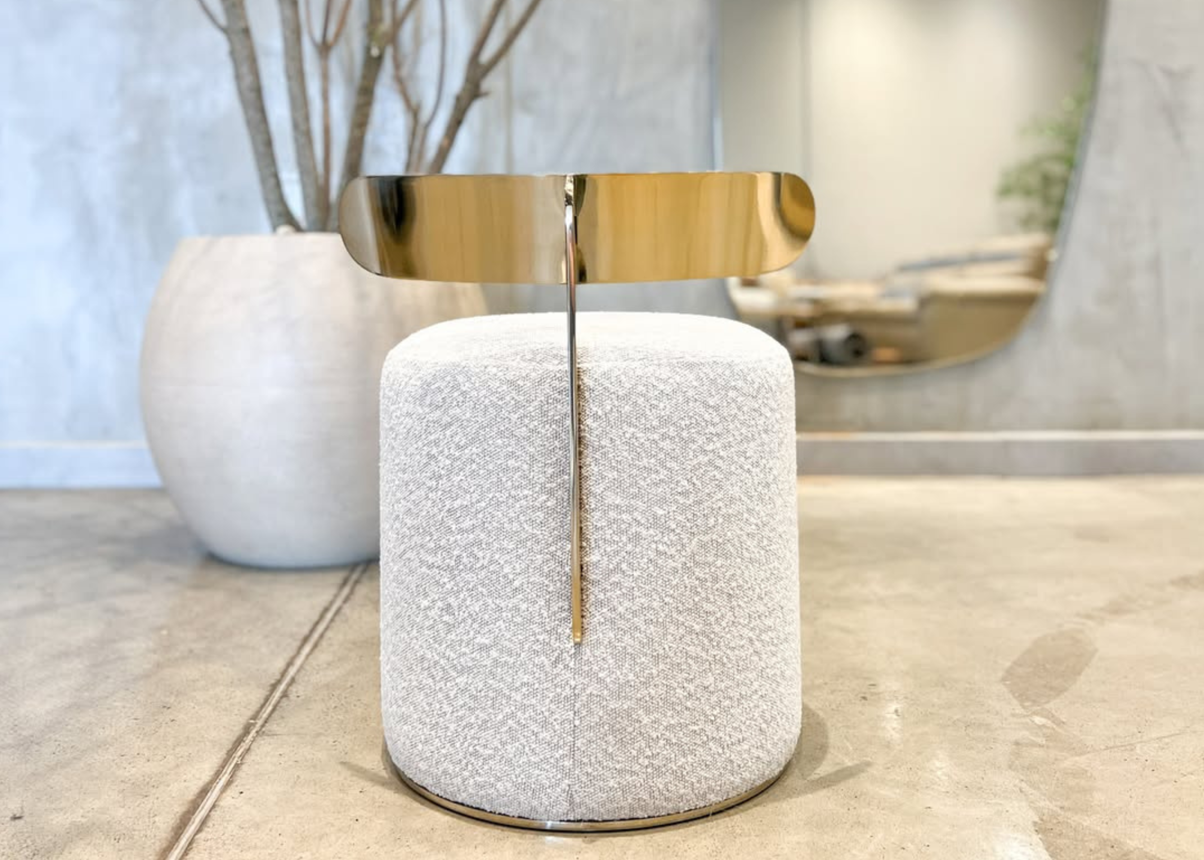 Puff redondo modelo Calla em bouclé branco com detalhe em inox dourado. Peça luxuosa e elegante para ambientes sofisticados.
