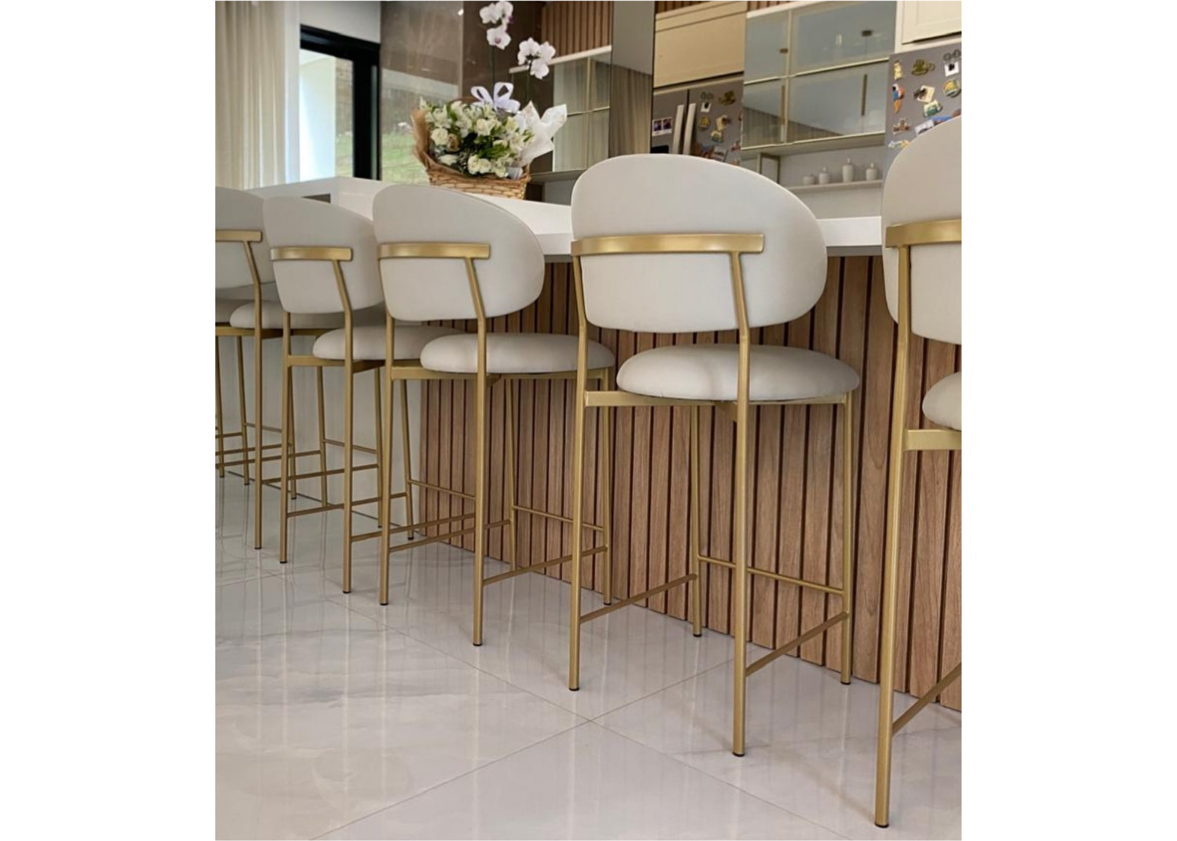 Banqueta Master com base dourada e estofado em tecido off-white, ambientada em cenário moderno. Móvel elegante e funcional para bancadas e áreas gourmet sofisticadas.