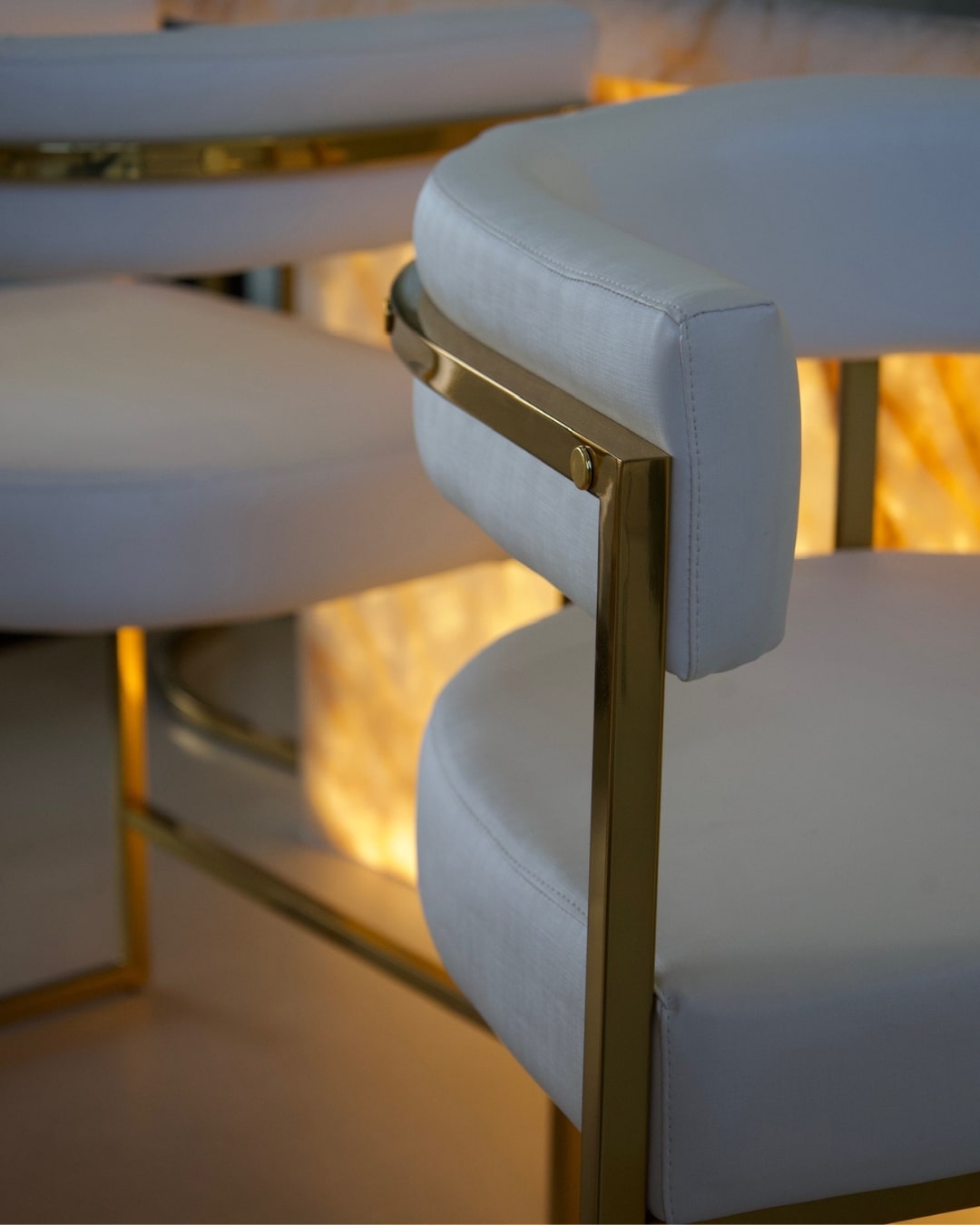 Banqueta com encosto curvo estofada, estrutura metálica dourada e design sofisticado.