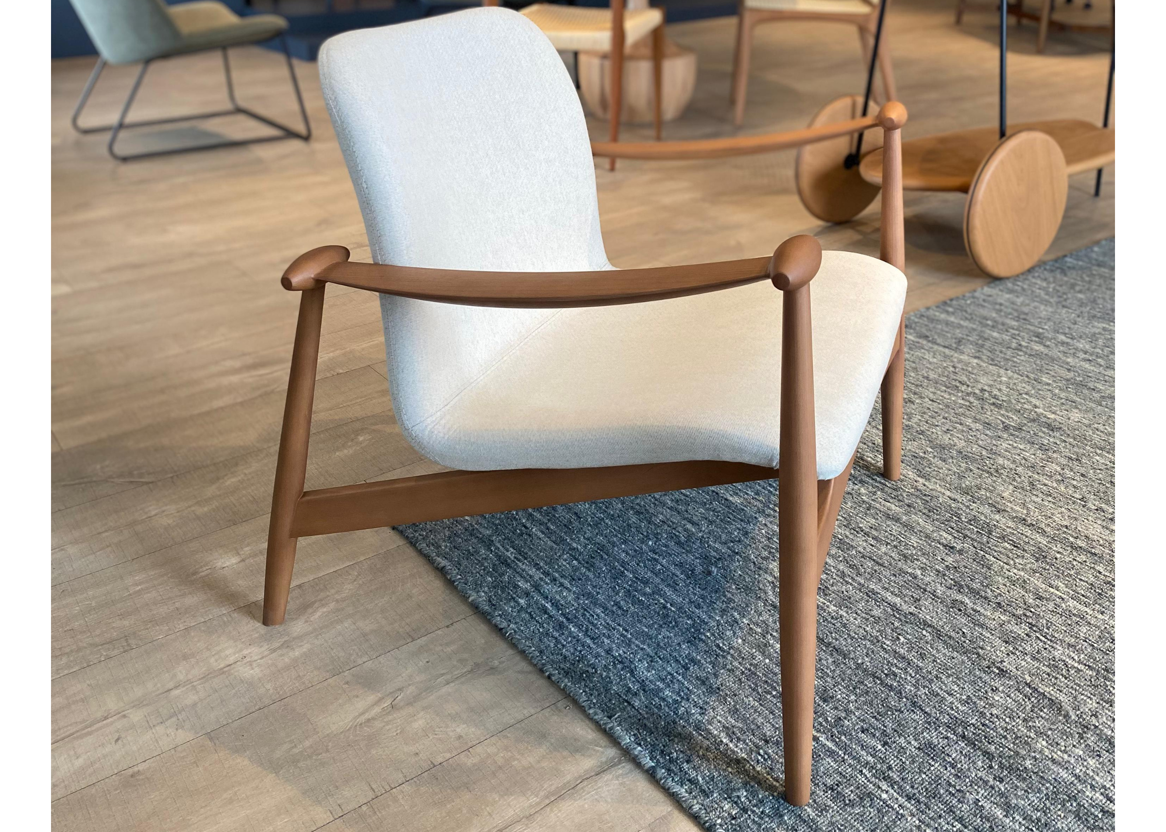 Poltrona estofada em linho com detalhes na base de madeira tingida, destacando elegância e conforto em um design contemporâneo.