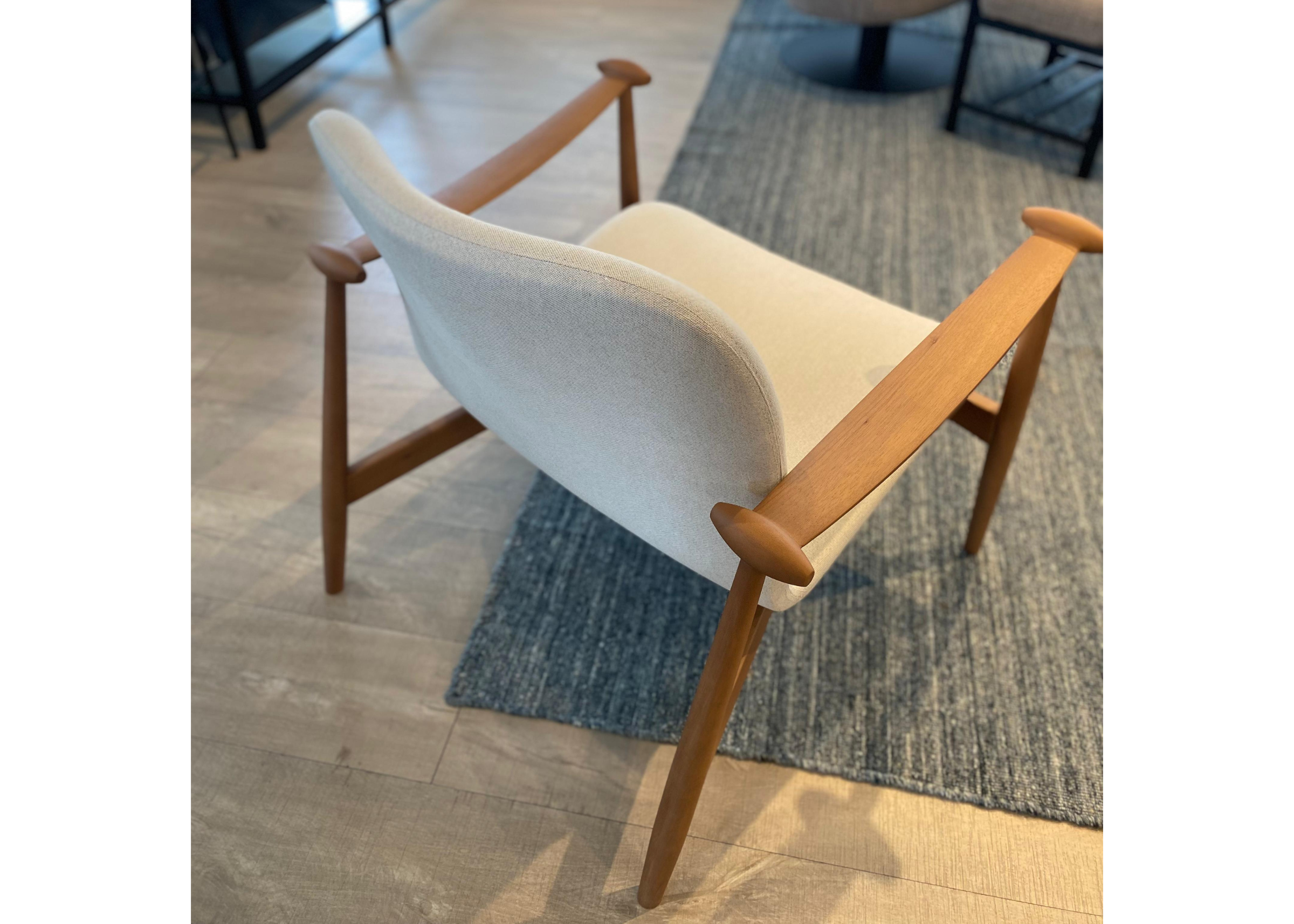 Poltrona estofada em linho com detalhes na base de madeira tingida, destacando elegância e conforto em um design contemporâneo.