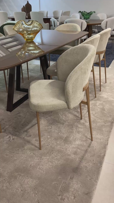 Cadeira Noa moderna estofada com base em aço carbono dourado e design sofisticado, ideal para sala de jantar de alto padrão.